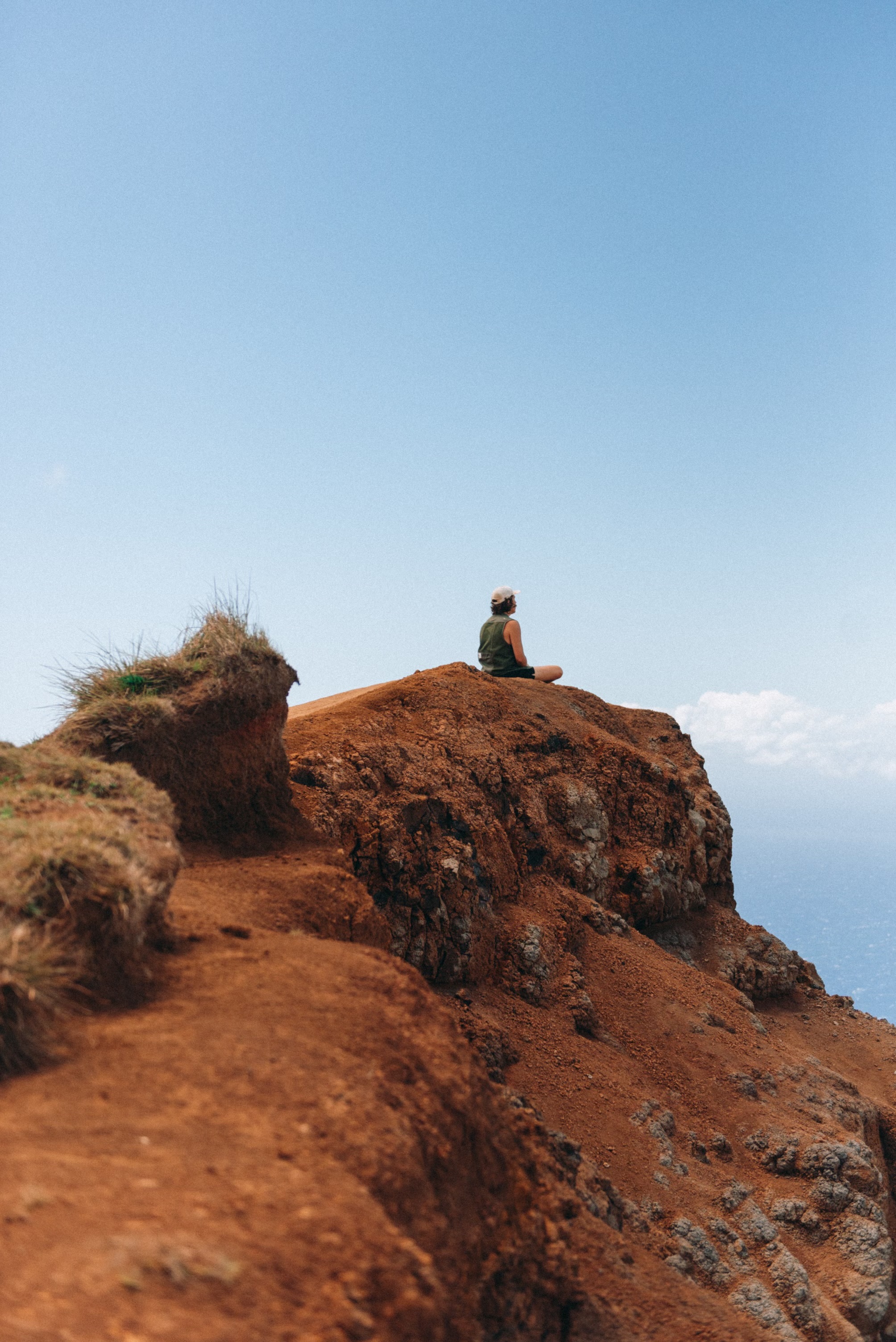 Person sitting contemplatively on a mountain cliff overlooking the ocean