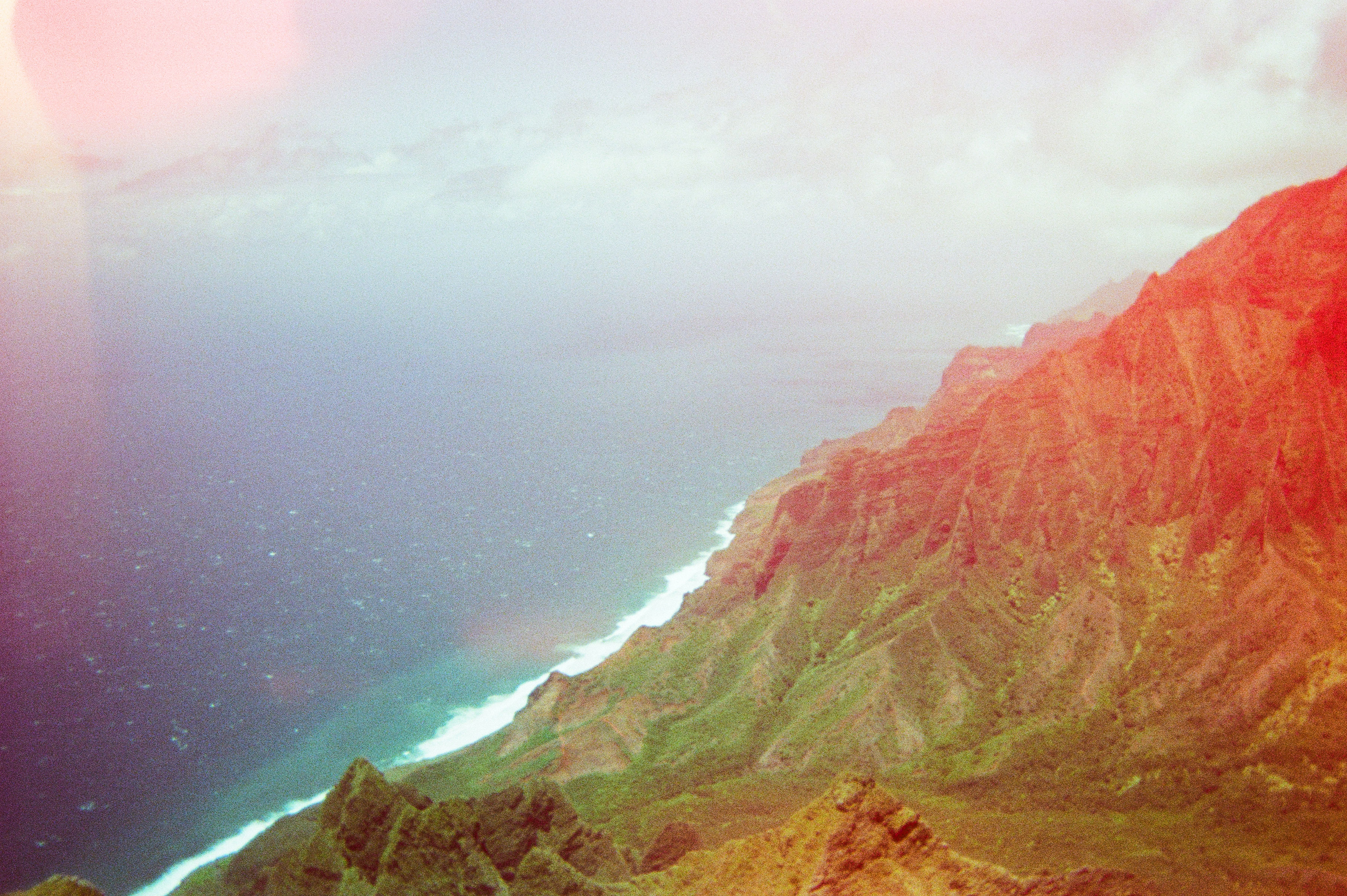 Aerial view of dramatic Hawaiian coastline with ocean meeting green cliffs in warm golden light